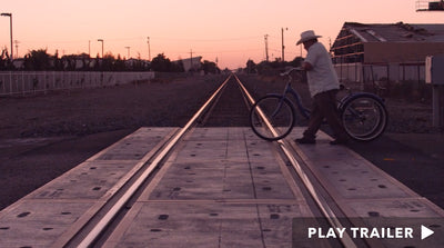 Trailer for documentary "Lupe Under The Sun" directed by Rodrigo Reyes. Man rolling his bike across train tracks. https://vimeo.com/170077110
