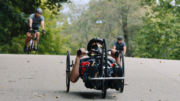 Still from the documentary "Bumps in the Road." Person riding a recumbent bike on a paved path with trees in the background