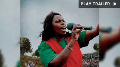 Trailer for the documentary "Our Land, Our Freedom" directed by Zippy Kimundu, A woman wearing a red and green shirt speaks into a microphone. https://vimeo.com/1102016731