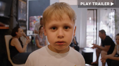 Trailer for documentary "Displaced" directed by Gil Cates, Jr.. Close up of little boy facing camera with family blurred in background. https://vimeo.com/830004841